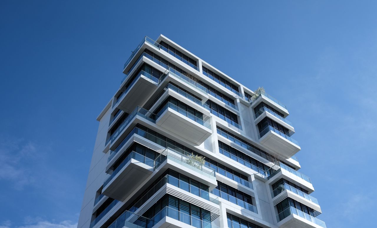 Striking low-angle shot of a modern condominium with unique balcony design and clear blue sky.